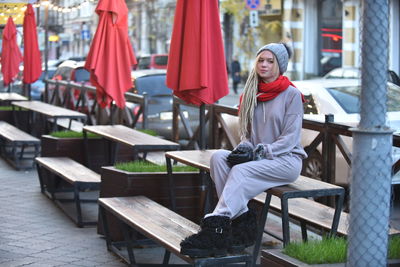 Portrait of woman in warm clothes while sitting on bench in city