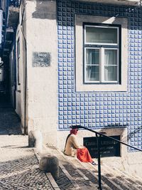 Woman sitting on footpath against building