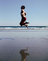 Full length of man jumping on beach against clear sky
