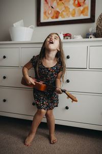 Full length of girl playing guitar while standing at home