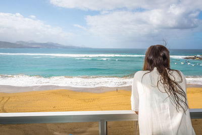 Rear view of woman standing on beach against sky