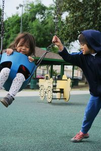 Boy pushing sister riding on swing in park