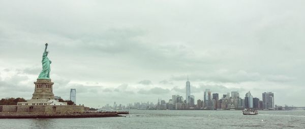 Statue of liberty by sea against cloudy sky