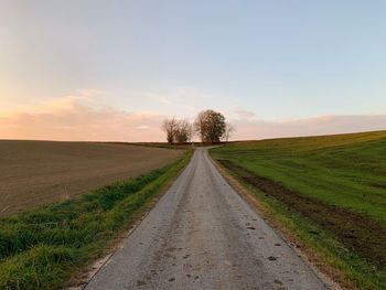 Empty road amidst field against sky