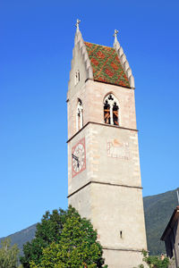 Low angle view of bell tower amidst buildings against clear blue sky