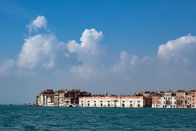 View of buildings by sea against cloudy sky