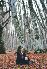 Smiling young woman sitting in forest during autumn