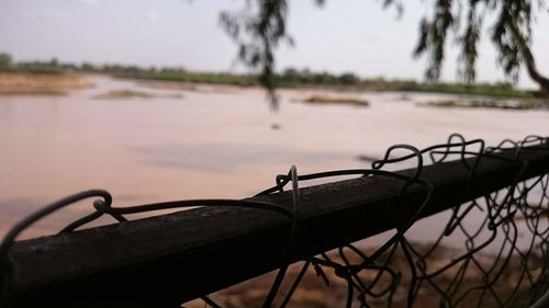 Close-up of railing by lake against sky