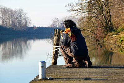 Rear view of woman crouching on pier over lake