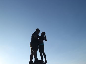 Low angle view of man and woman standing against clear sky