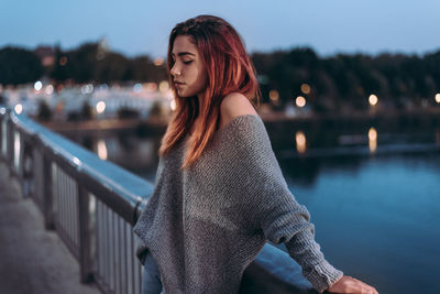 Beautiful young woman on footbridge over river in city at night