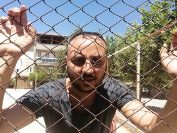 Portrait of young man seen through chainlink fence