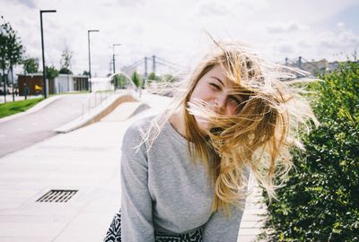 Portrait of a young woman with windy blonde hair on road