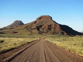 Dirt road amidst mountains against clear sky