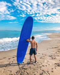 Rear view of shirtless man with surfboard standing at beach