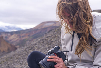 Woman sitting looking down at camera in the wind, in landmannalaugar