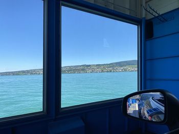 View of sea against clear blue sky seen through window