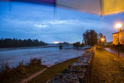 Road by trees against sky at dusk