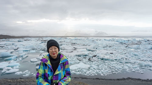 Portrait of smiling woman by glacier in sea during winter