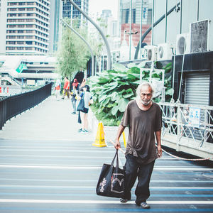 Senior man carrying bag while walking on city street