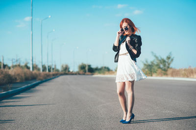 Woman with umbrella standing on road against the sky