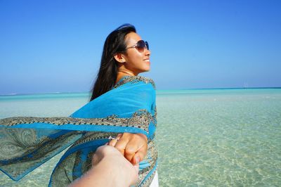 Couple holding hands while standing in sea against clear sky