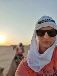 Portrait of man in sunglasses wearing headscarf against sky during sunset