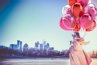 Young woman standing with balloons against sky in city