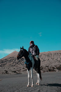 Full length of man riding horse on desert against sky