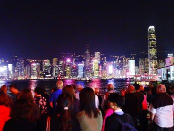 People looking at illuminated modern buildings in city at night