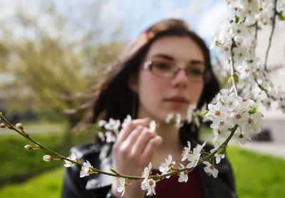 Portrait of young woman with pink flowers against trees
