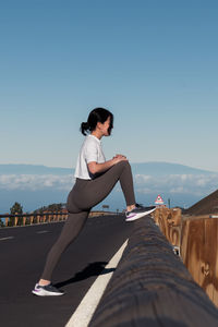 Woman sitting on retaining wall against clear sky