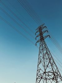 Low angle view of electricity pylon against clear blue sky