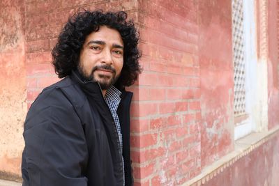 Portrait of young man standing by brick wall