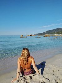 Rear view of woman sitting on beach against clear sky