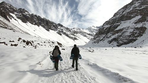 Rear view of people walking on snowcapped mountain against sky