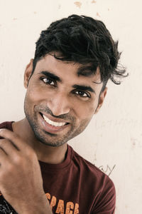 Close-up portrait of smiling young man against wall