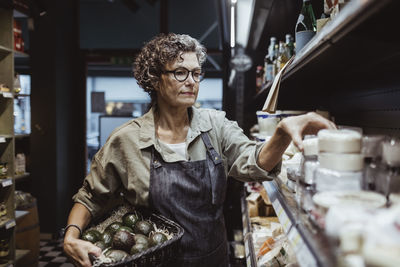 Mature male entrepreneur arranging product on rack at delicatessen store