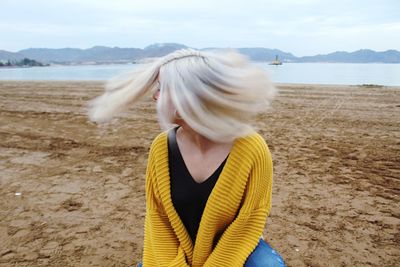 Woman with tousled hair sitting at beach against sky