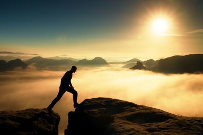 Hiker in black is jumping between the rocky peaks. wonderful daybreak in rocks. miracle of nature