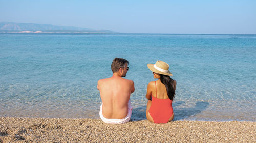 Rear view of woman sitting at beach against sky