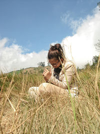 Rear view of man sitting on field against sky