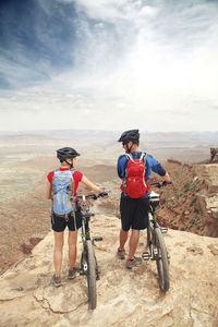 Rear view of couple standing with bicycles on cliff