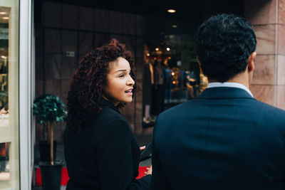 Rear view of businesswoman talking with businessman while walking against building in city