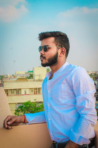 Young man wearing sunglasses sitting against sky