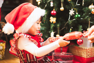 Cropped hand of woman giving gift to girl by christmas tree