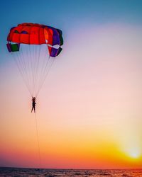 Silhouette person paragliding over sea against sky during sunset