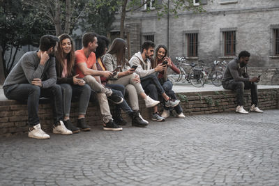 Friends sitting on retaining wall in city