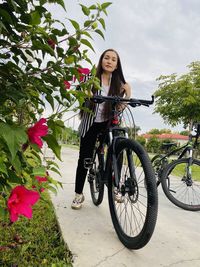 Woman standing on bicycle by flowering plants