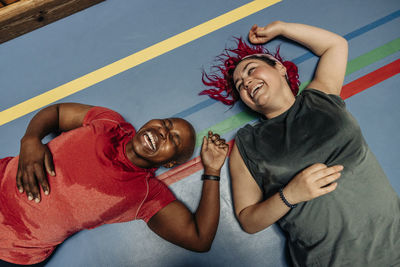 High angle view of female athletes laughing while lying on safety mat at sports court